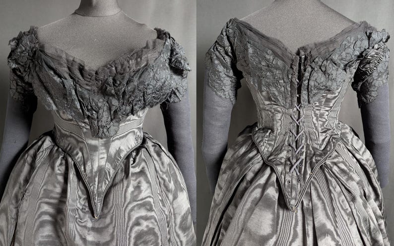 May include: A vintage gray dress with a fitted bodice and a full skirt. The dress features intricate lace detailing on the sleeves and neckline. The back of the dress has a corset-style closure. The fabric has a subtle striped pattern.