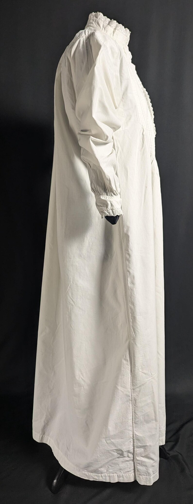 May include: A long, white nightgown with a high neckline and long sleeves. The nightgown features delicate lace trim around the collar and cuffs. The fabric appears to be a lightweight cotton or linen.
