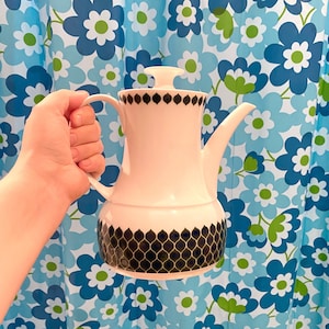 May include: A white ceramic coffee pot with a black and white geometric pattern. The pot has a lid and a handle.