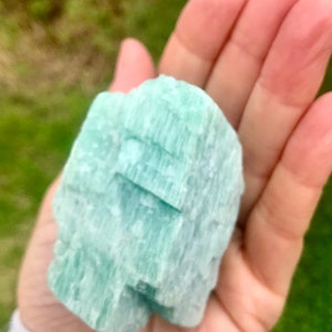 May include: A light green, naturally formed crystal with a striated texture. The crystal is smooth and polished, with a slightly translucent appearance.