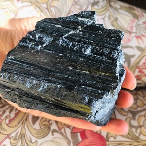 May include: A large, black, rough-hewn piece of black tourmaline crystal. The crystal has a striated, layered texture.