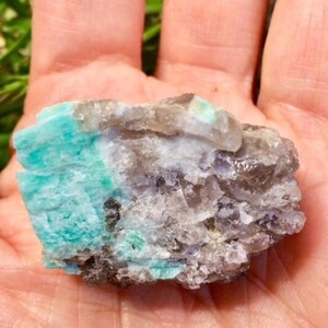 May include: A raw, natural crystal cluster with a combination of clear, gray, and green colors. The green portion of the crystal is a vibrant emerald green.