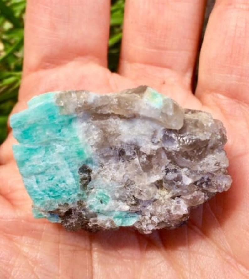 May include: A raw, natural crystal cluster with a combination of clear, gray, and green colors. The green portion of the crystal is a vibrant emerald green.