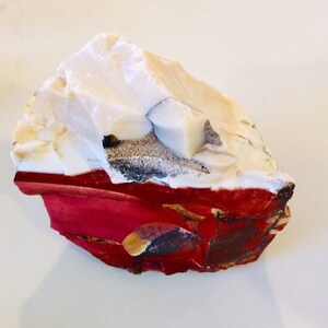 May include: A rough, white and red rock with a layered appearance. The top layer is white with a rough, textured surface. The bottom layer is red with a smooth, polished surface.