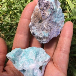 May include: Two rough, natural, green and white amazonite crystals. The larger crystal has a dark gray, almost black, mineral inclusion.