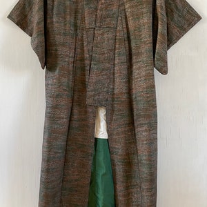 May include: A brown and green patterned kimono with a green lining. The kimono is hanging on a white wall.