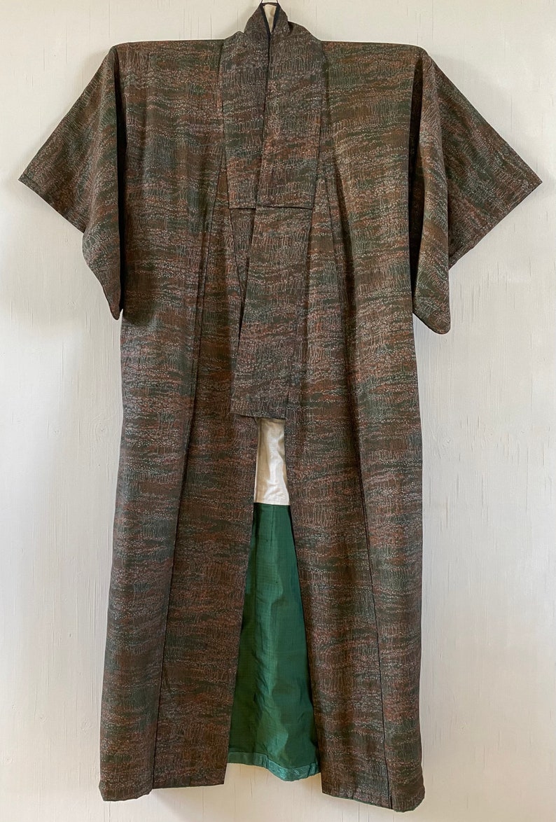 May include: A brown and green patterned kimono with a green lining. The kimono is hanging on a white wall.