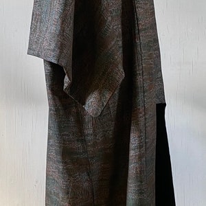 May include: A long, brown and green patterned coat with a short sleeve. The coat is on a mannequin and is standing on a wooden floor.