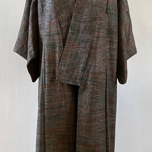 May include: A long, brown and green patterned robe with a wide collar and long sleeves. The robe is open in the front and is being displayed on a mannequin.