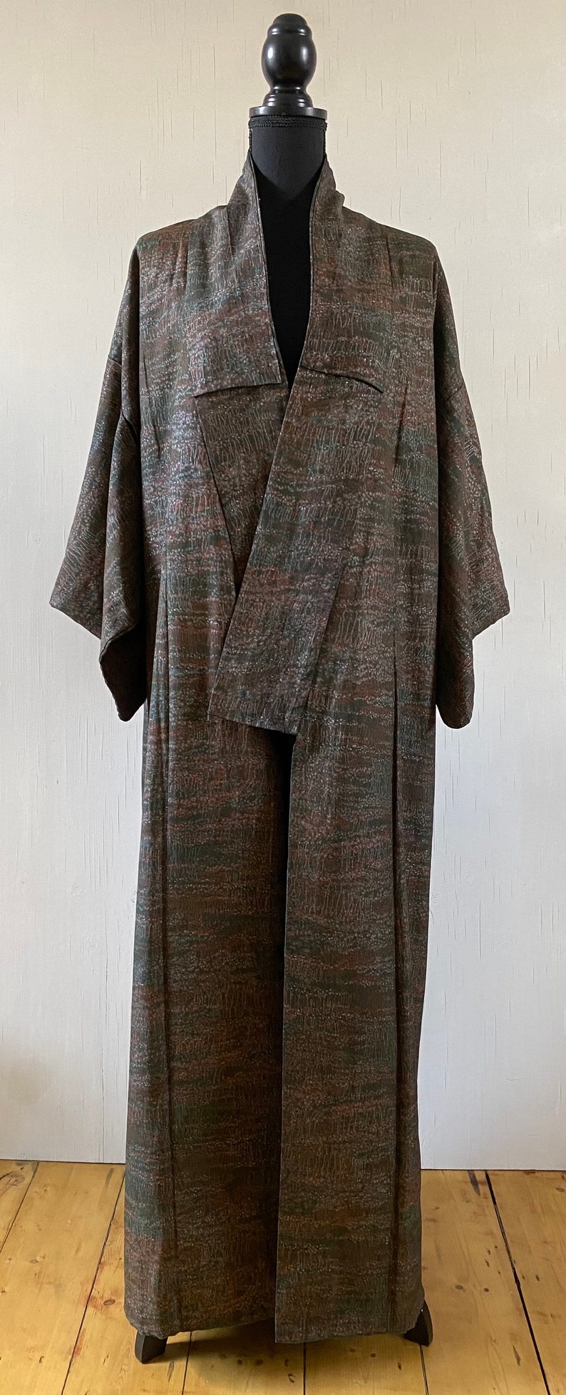 May include: A long, brown and green patterned robe with a wide collar and long sleeves. The robe is open in the front and is being displayed on a mannequin.