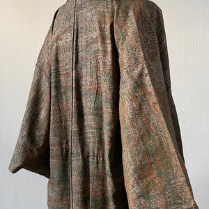 May include: A brown and green patterned kimono with a black collar and a long sleeve. The kimono is displayed on a mannequin.