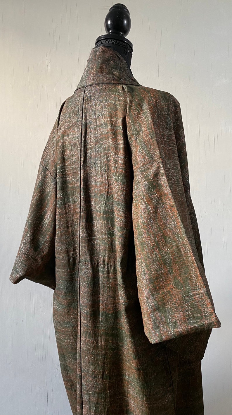 May include: A brown and green patterned kimono with a black collar and a long sleeve. The kimono is displayed on a mannequin.