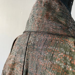 May include: Close-up of the back of a green, orange, and white patterned jacket. The jacket has a high collar and is made of a soft, textured fabric.