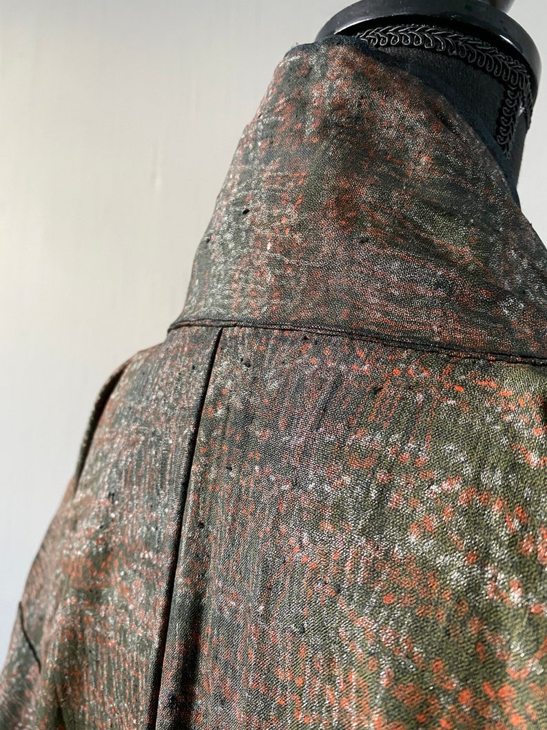 May include: Close-up of the back of a green, orange, and white patterned jacket. The jacket has a high collar and is made of a soft, textured fabric.