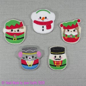 May include: Five embroidered patches featuring holiday characters: a green elf, a white snowman with a red scarf, a second elf in a red hat, a grey mouse in a soldier uniform, and a nutcracker figure with a black hat and green jacket.
