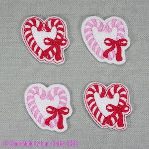 May include: Four embroidered patches shaped like hearts formed by candy canes. Two patches feature red and white stripes with red bows, while two patches feature pink and white stripes with red bows. The patches have a white glittery centre.