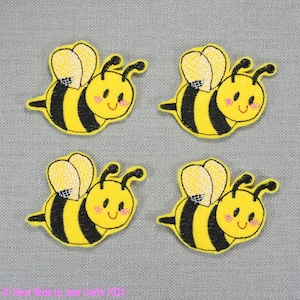 May include: Four yellow felt bee appliques with black stripes and white wings. Each bee has a smiling face with pink cheeks.