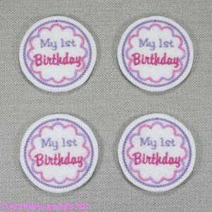 May include: Four white felt circles with pink and purple embroidery. Each circle says "My 1st Birthday" in pink and purple lettering.