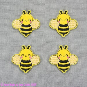 May include: Four yellow felt bee appliques with black stripes and pink cheeks. Each bee has a smiling face and small, yellow wings.