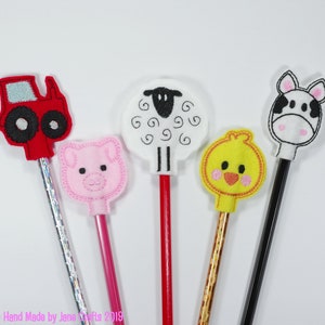 May include: Five colourful pencil toppers with farm animal designs. The toppers include a red tractor, a pink pig, a white sheep, a yellow chick, and a black and white cow.
