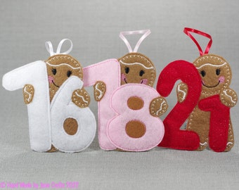 May include: Three felt gingerbread ornaments, each with a different number. The first ornament is white with the number 16, the second is pink with the number 18, and the third is red with the number 21.