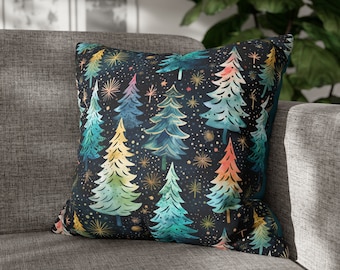 May include: Square throw pillow with a dark background and a pattern of colorful Christmas trees in shades of green, blue, yellow, and red. The trees are interspersed with gold starbursts and white dots. The pillow is resting on a gray sofa.