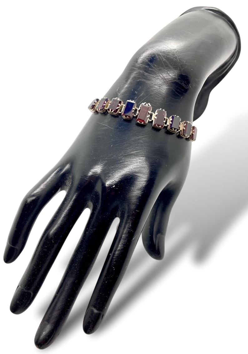 May include: A silver bracelet with a row of rectangular red and blue gemstones.