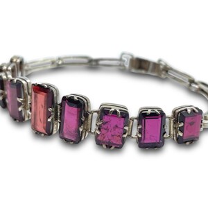 May include: A silver bracelet with a chain link design and rectangular pink and purple gemstones.