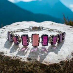 May include: A silver bracelet with a chain link design and rectangular purple and pink gemstones.