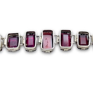 May include: A silver bracelet with a row of rectangular, dark purple gemstones.