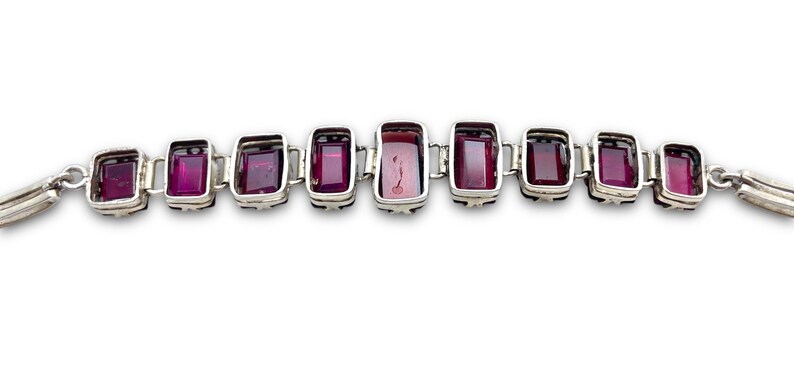 May include: A silver bracelet with a row of rectangular, dark purple gemstones.