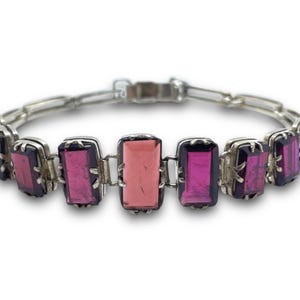 May include: A silver bracelet with a chain link design and rectangular pink and purple gemstones.