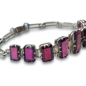 May include: A silver bracelet with a chain link design and rectangular purple gemstones.