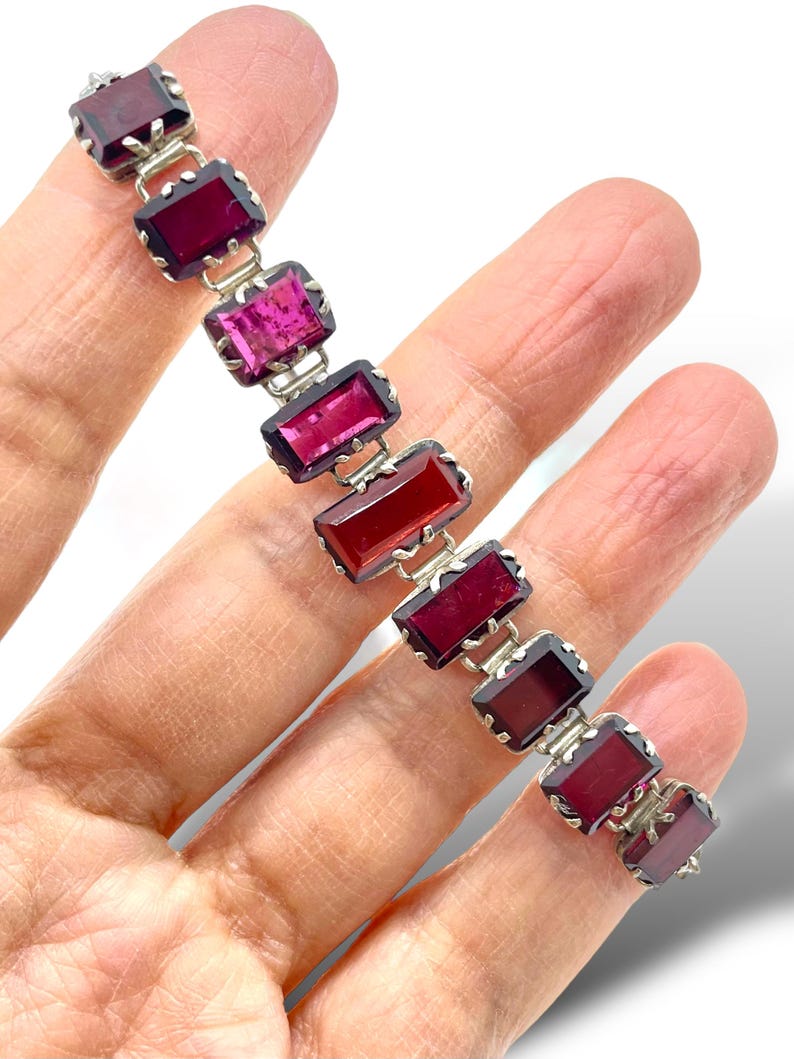 May include: A silver bracelet with a row of rectangular red, pink, and purple gemstones. The gemstones are set in silver and have a faceted cut.