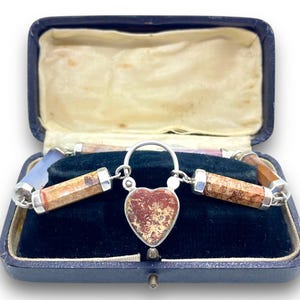 May include: A vintage silver necklace with a heart-shaped pendant and cylindrical stone beads, displayed in a blue velvet-lined box. The pendant and beads feature earthy tones of brown, red, and beige.