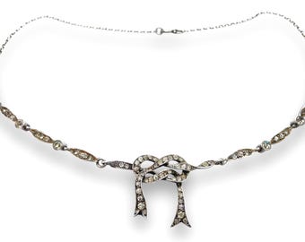 May include: A silver necklace with a crystal-encrusted bow knot pendant.