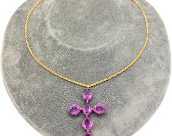 May include: A gold chain necklace with a pendant in the shape of a cross. The cross is made of multiple oval-shaped purple gemstones.