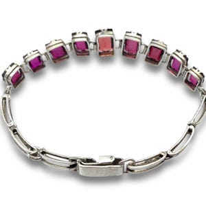 May include: A silver bracelet with a row of pink and purple rectangular gemstones. The bracelet has a silver clasp.