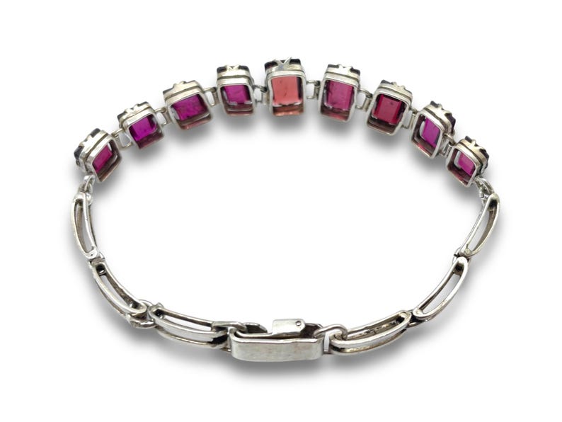 May include: A silver bracelet with a row of pink and purple rectangular gemstones. The bracelet has a silver clasp.