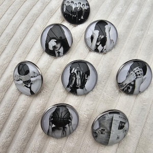 Op de afbeelding: Een verzameling van zeven ronde buttons met zwart-wit fotoprints. De ontwerpen bevatten een groepsportret, personen met capuchons, een persoon die een basketbal vasthoudt en een persoon die een krant leest.