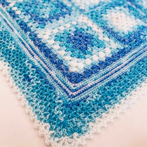 Puede incluir: Una manta de bebé de ganchillo en tonos azules y blancos con un borde festoneado.