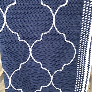 Könnte beinhalten: Eine marineblaue gehäkelte Decke mit einem weißen geometrischen Muster und einem weißen gehäkelten Rand.