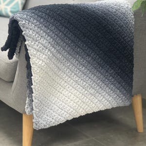 Pode incluir: Uma manta macia de ombre cinza e preto drapeada sobre um sofá com pernas de madeira.