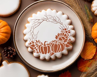 May include: A decorated sugar cookie with a white base and a brown pumpkin and floral design, on a white plate with a gold rim. The cookie is surrounded by other cookies, pumpkins, and autumn leaves.