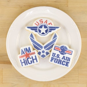 Könnte beinhalten: Vier verzierte Zuckerkekse mit blauem und rotem Zuckerguss. Die Kekse zeigen die Worte "USAF", "Aim High", "U.S. Air Force" und ein blaues Air Force-Logo.