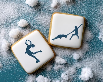 May include: Two square biscuits with white icing and dark blue silhouettes of ice skaters. One biscuit features a solo skater in a spin, while the other shows a pair of skaters performing a move. The biscuits are surrounded by white sugar crystals.
