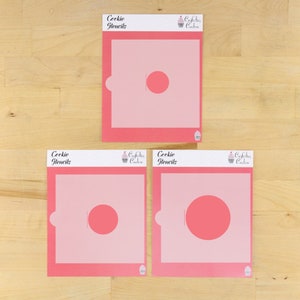 May include: Three pink cookie stencils with the text "Cookie Stencils" and a cupcake logo. The stencils are different sizes and feature a circle cutout.