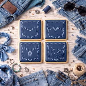 May include: Four square cookies decorated with blue icing and white stitching to resemble denim jean pockets. The cookies are arranged on a light wood surface, surrounded by denim fabric, sunglasses, and sewing notions.