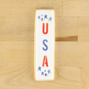 Könnte beinhalten: Ein weißer Keks, der mit blauen Sternen und dem Wort "USA" in roten und blauen Buchstaben verziert ist.