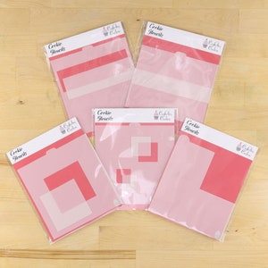 May include: Five pink cookie stencils with the text "Cookie Stencils" and a cupcake logo. The stencils are packaged in clear plastic sleeves.